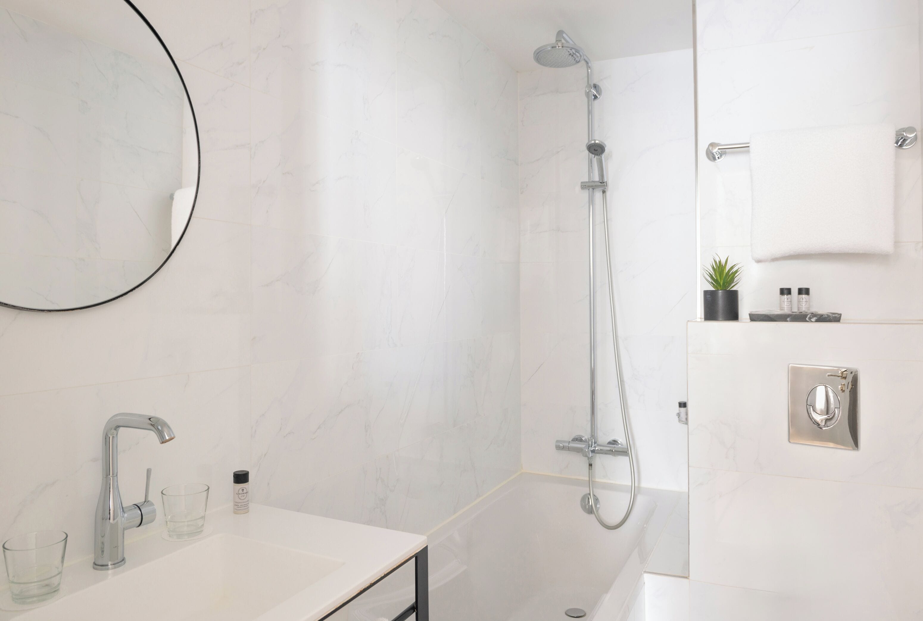 A modern bathroom with a white marble sink, a handheld showerhead, and a towel rack.