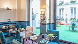 Un espace repas avec des tables et des chaises, une vue sur la cour et une bibliothèque en arrière-plan.