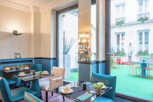 Un espace repas avec des tables et des chaises, une vue sur la cour et une bibliothèque en arrière-plan.