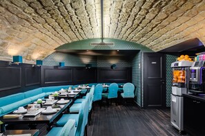 A restaurant with a long counter, teal upholstered booths, and a stone ceiling. - Hôtel Monceau Elysées (Paris)
