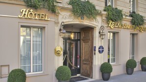 A hotel entrance with a large sign reading "HOTEL" and another sign for "RELAIS SAUTE L'ACOUF". There are potted plants in front of the entrance and a door with a sign indicating the hotel's name.