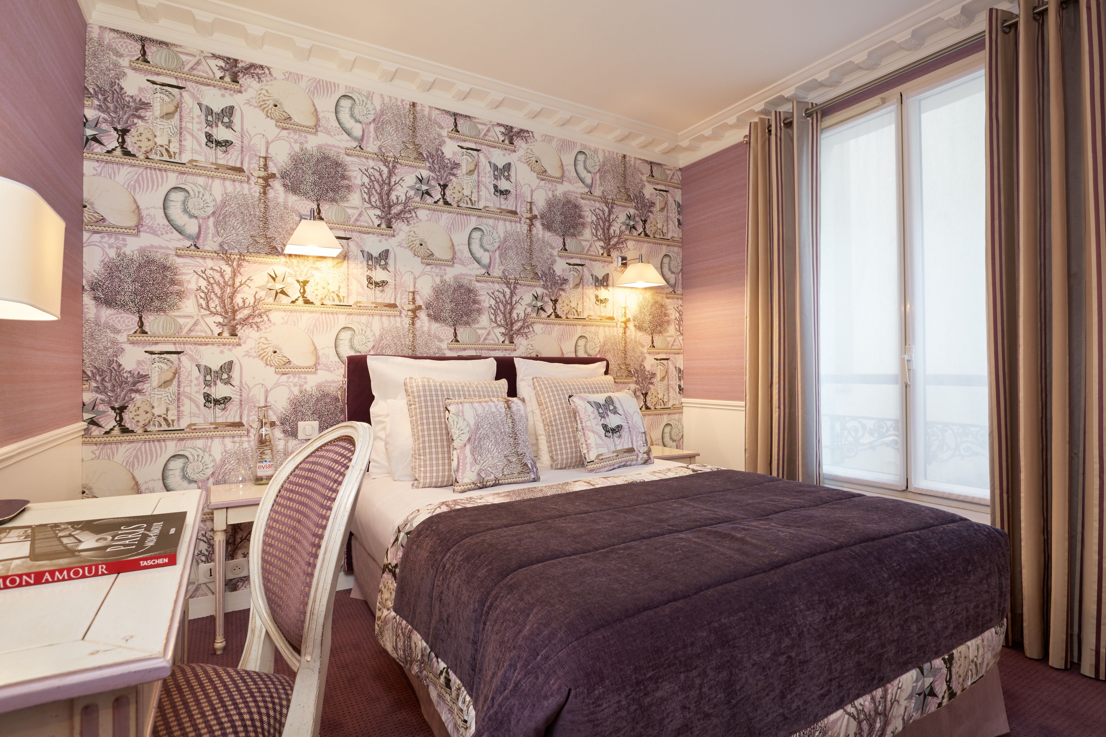 A hotel room with a large bed, two bedside lamps, a table with a book, and a view of the outdoors through a window.