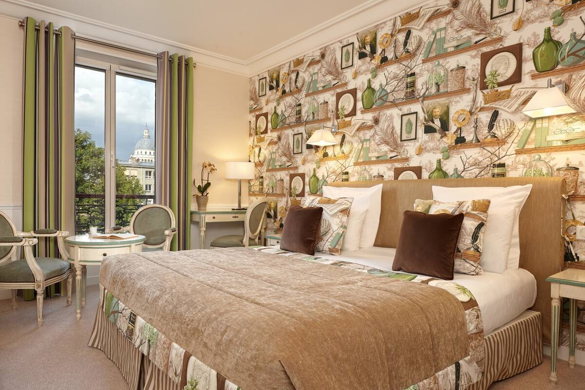 Habitación de hotel con una cama grande, un escritorio y una silla. Hay una ventana con cortinas y una pared decorada con marcos y jarrones.