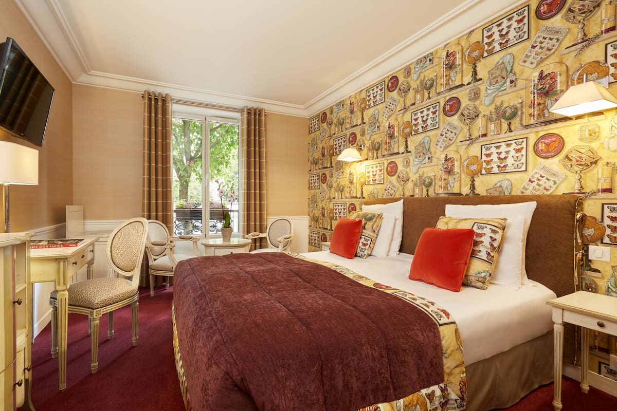 Habitación de hotel con una cama grande, un escritorio, una silla y un ventanal con cortinas.