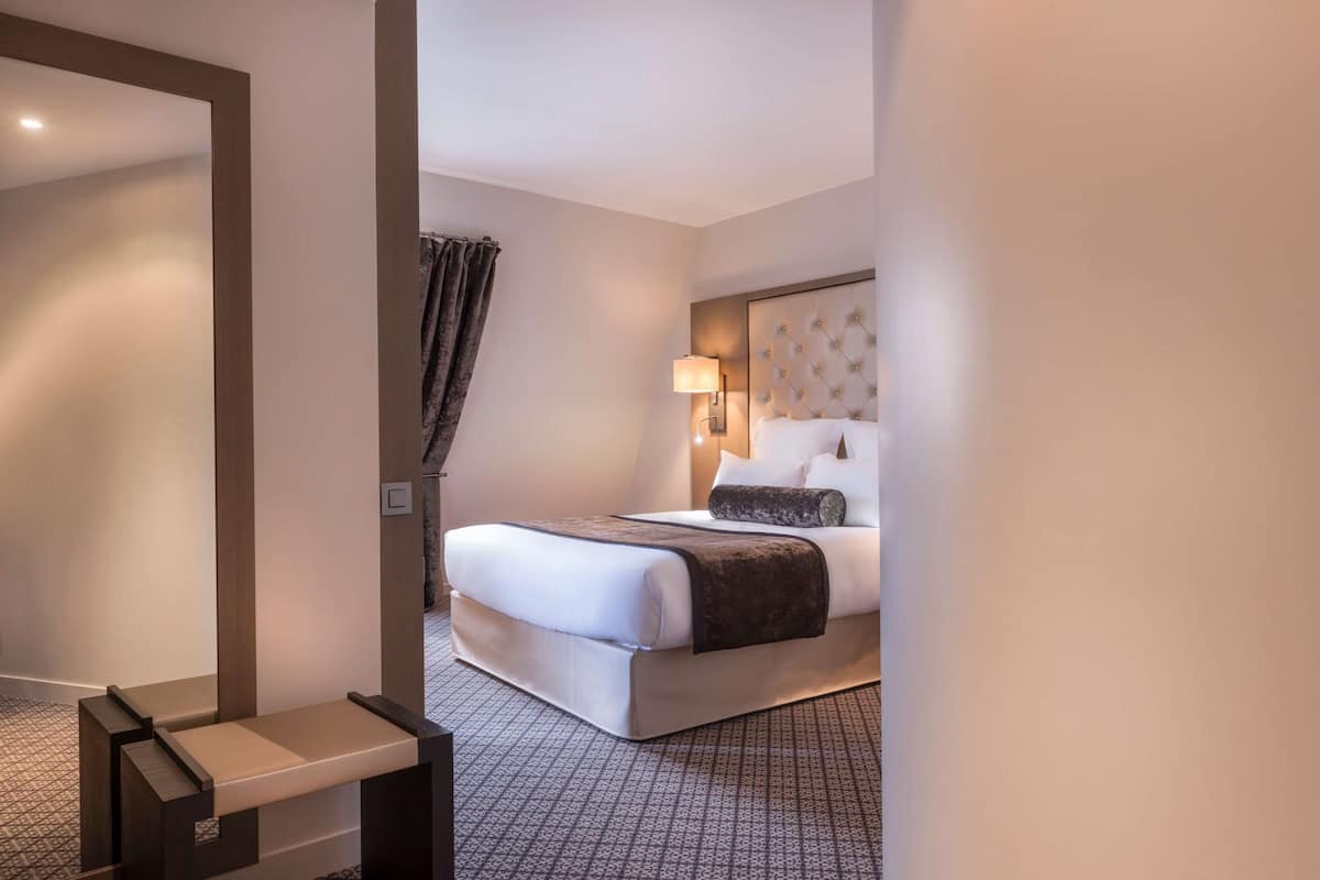 A hotel room with a large bed, a bedside table, a lamp, and a patterned carpet.