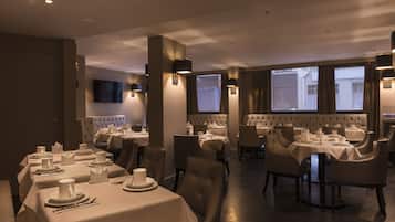 En restaurang med flera bord och stolar, där varje bord är dukat med tallrikar, bestick och glas.