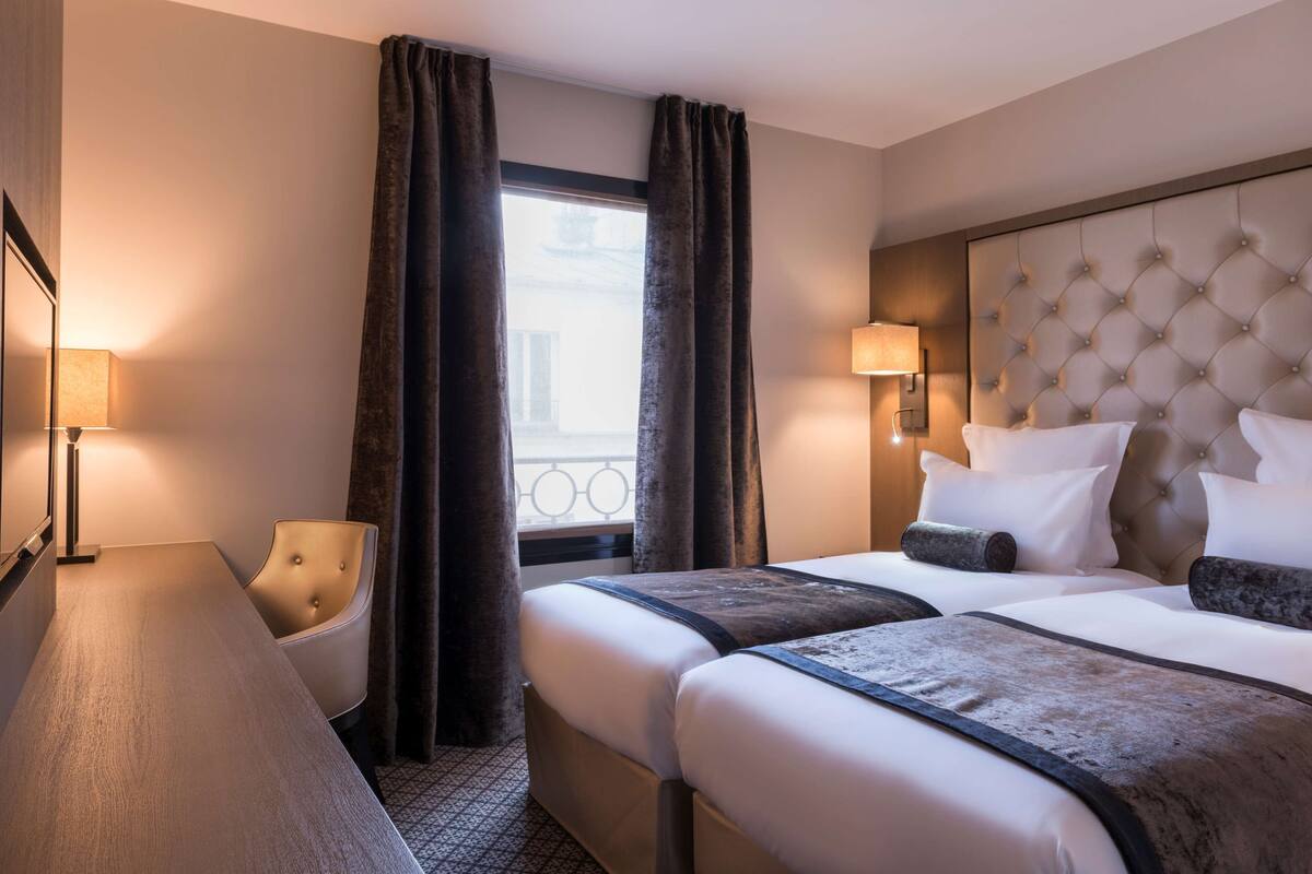 A hotel room with a bed, a chair, a desk, and a window with curtains.