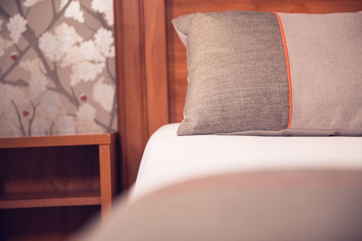 Un lit bien fait, avec un oreiller gris et un bordure orange.
