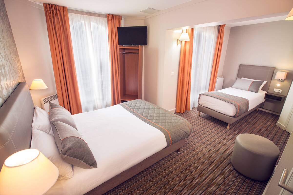 Une chambre d’hôtel avec deux lits, une télévision, une table de chevet avec une lampe et une armoire.