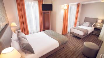 A hotel room with two beds, a TV, a bedside table with a lamp, and a wardrobe.