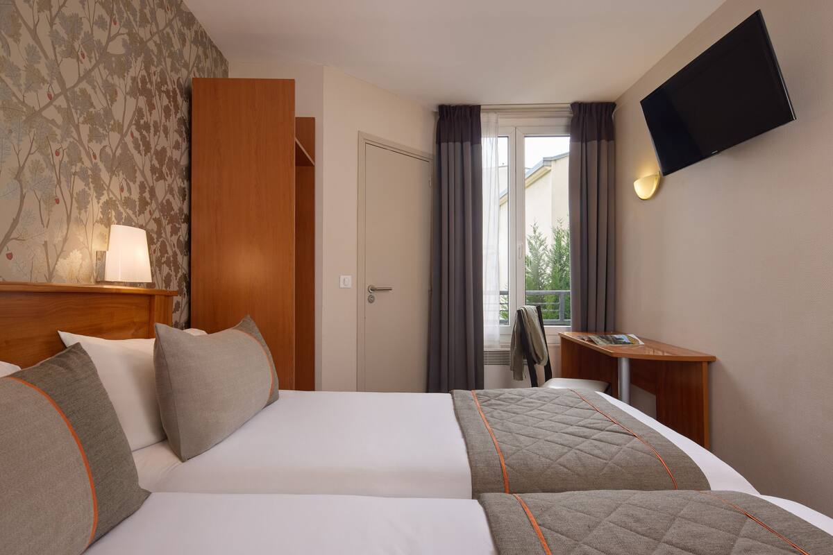 Une chambre d’hôtel équipée d’un lit, d’un bureau, d’une télévision et offrant une vue sur l’extérieur.