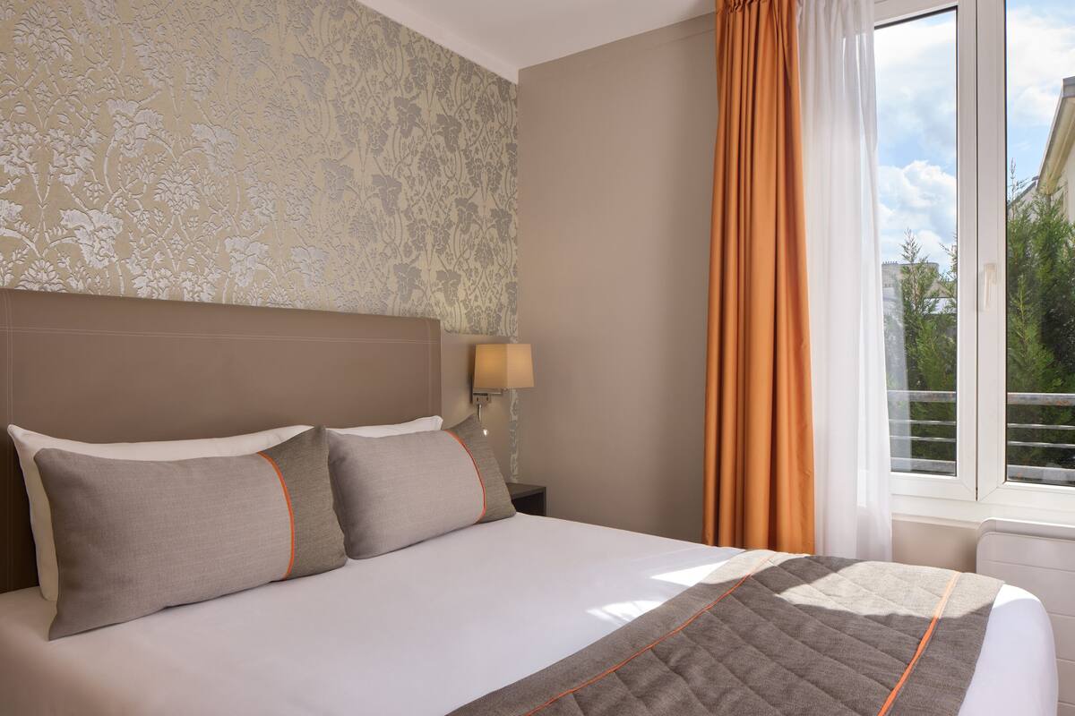 Une chambre d’hôtel avec un grand lit, une table de chevet, une lampe et une fenêtre avec des rideaux.