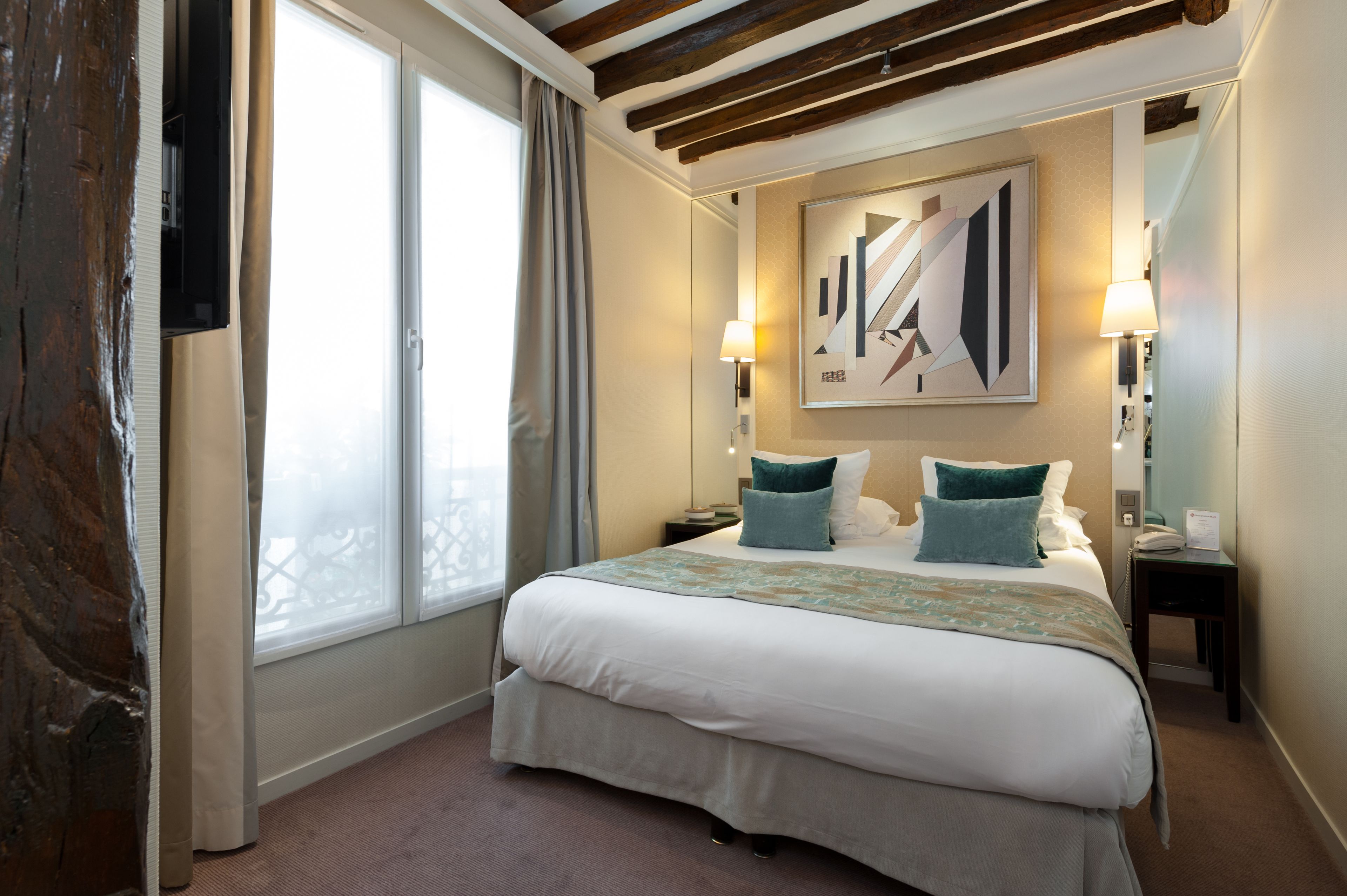A hotel room with a large bed, two bedside tables, a wall-mounted TV, and a window with curtains.