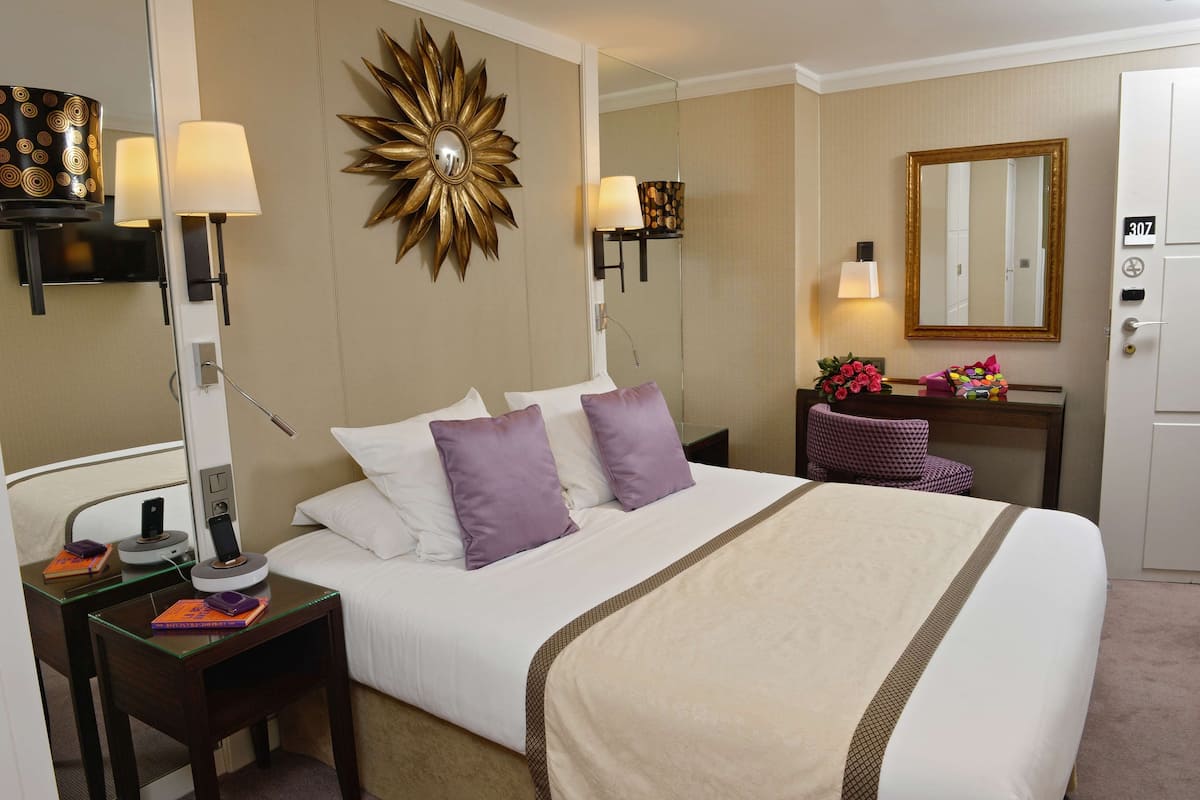 A hotel room with a large bed, two bedside tables with lamps, a vanity with a mirror, and a door with a number plate.