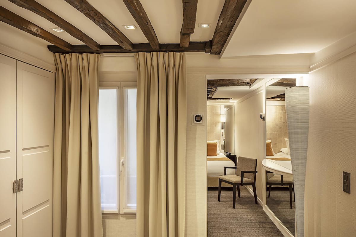 A hotel room with a wooden ceiling, a bed, a chair, and a bathroom visible through an open door.