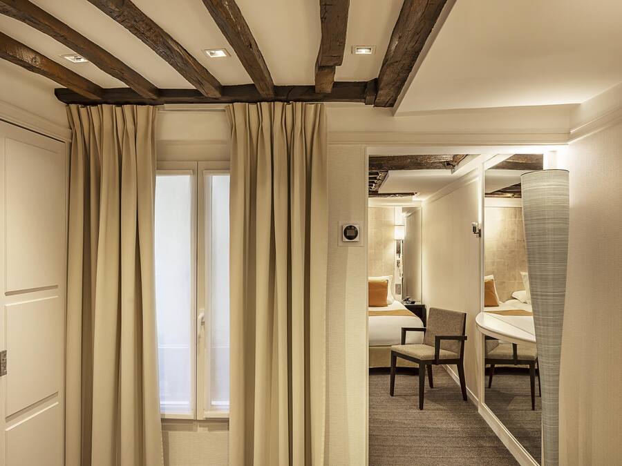 Habitación de hotel con techo de madera, una cama, una silla y un baño visible a través de una puerta abierta.