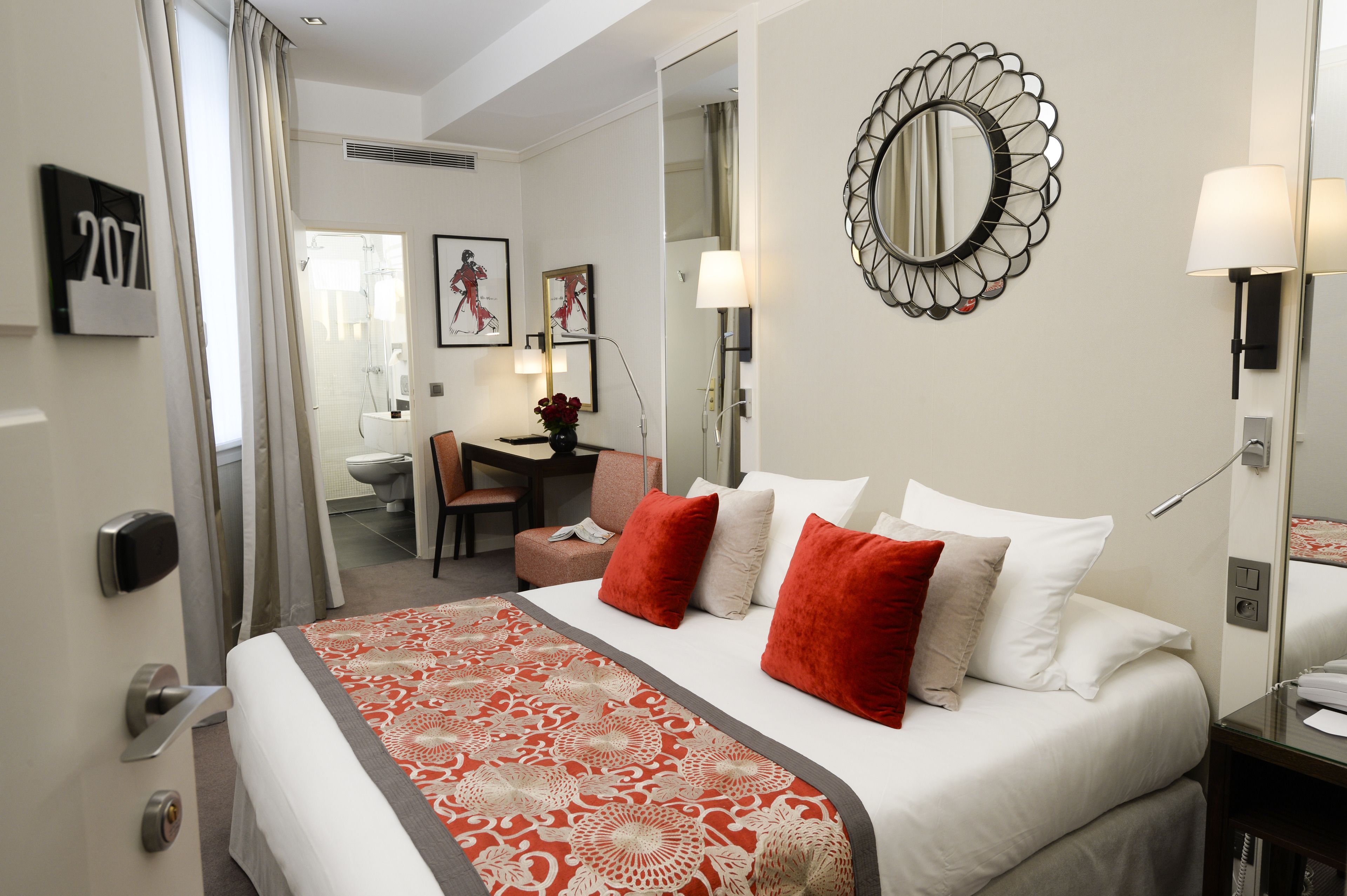 Habitación de hotel con cama, escritorio, silla, baño y espejo.
