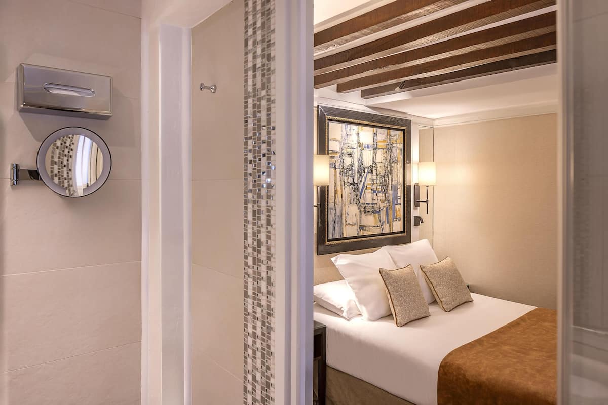 A hotel room with a bed, a large framed abstract painting, a round mirror, and a wall-mounted light fixture.