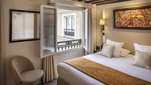 Une chambre d’hôtel avec un lit, une chaise, une fenêtre donnant sur un balcon, un tableau au mur et une lampe.