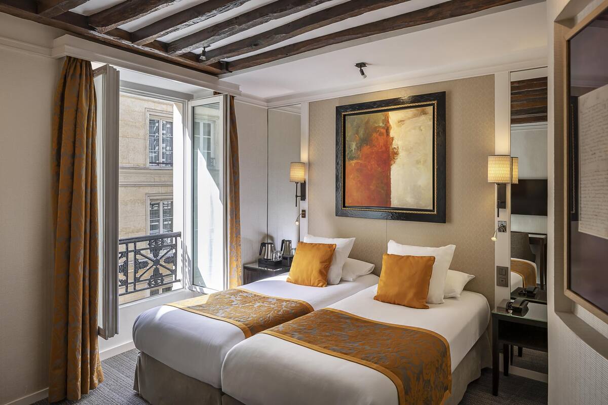 A hotel room with two beds, a balcony, a painting, and a desk with a lamp.