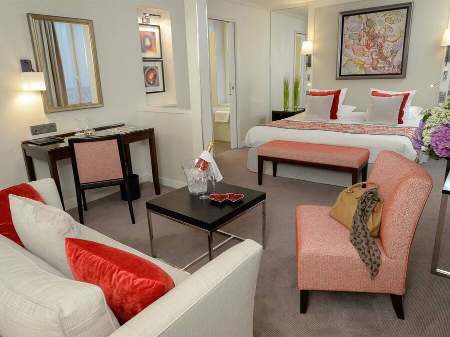 Une chambre d’hôtel équipée d’un canapé, d’un fauteuil, d’un lit, d’une table de chevet et d’un petit bureau avec une chaise.