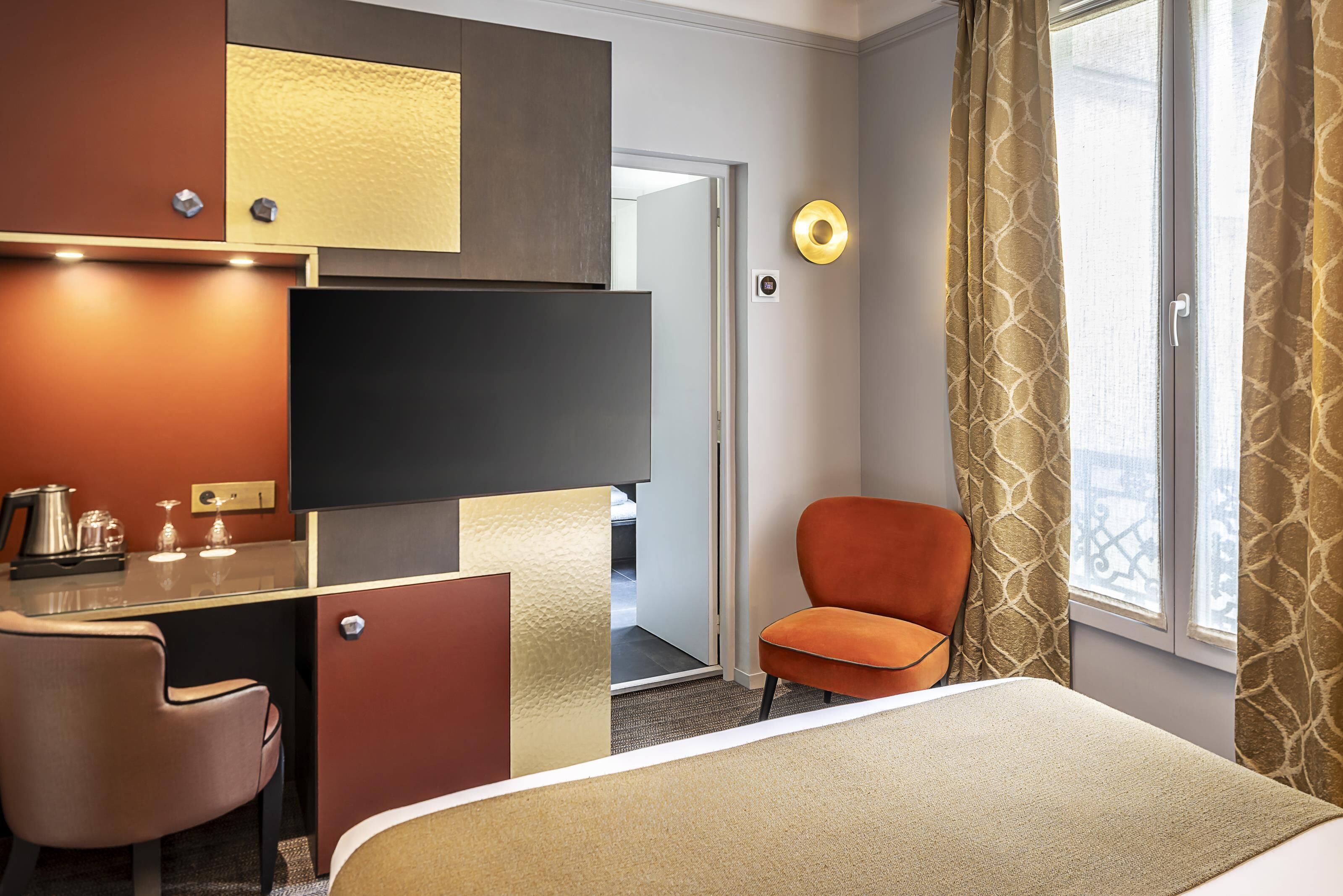 A hotel room with a bed, a desk with a chair, a television, and a window with curtains.