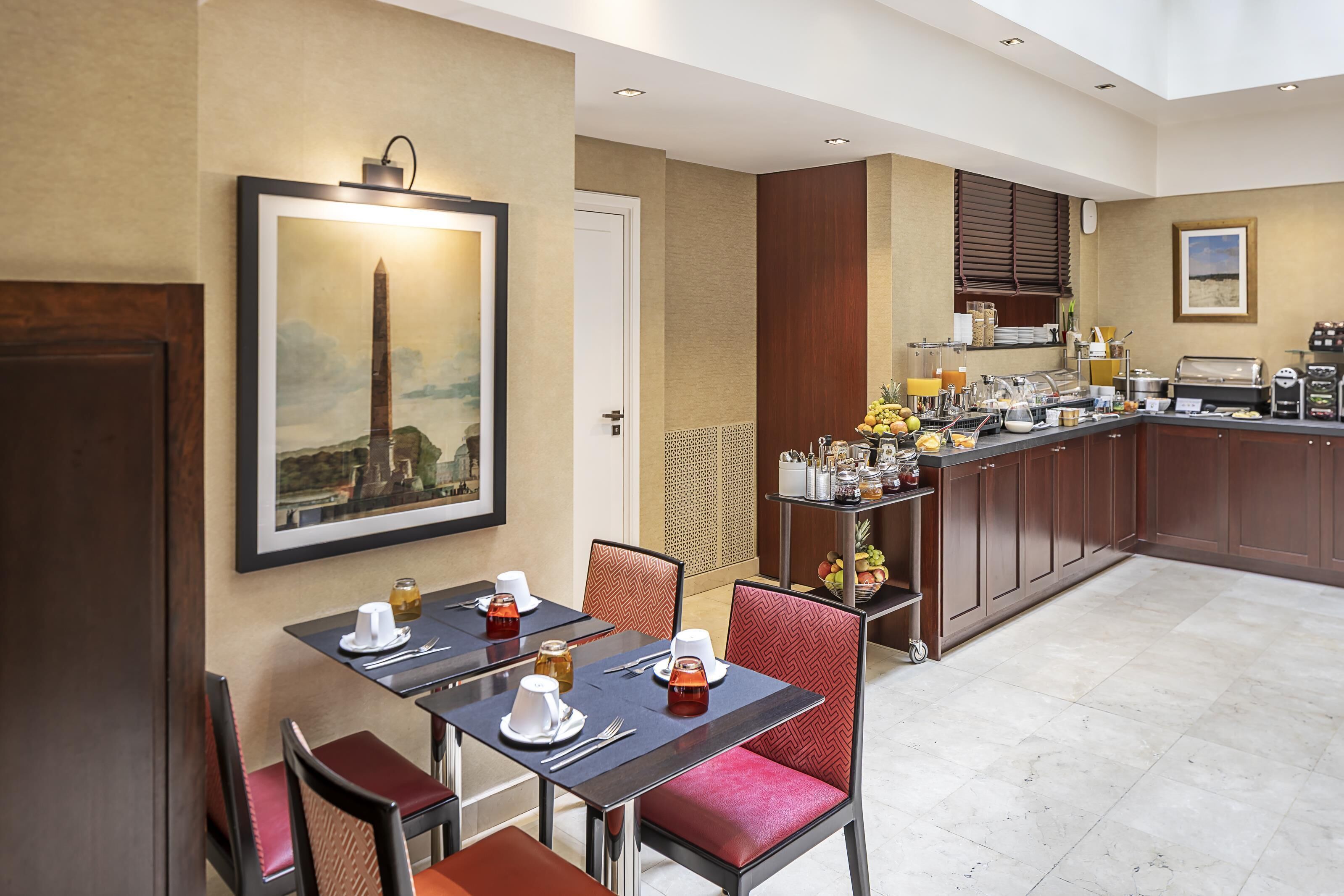 Een restaurantgedeelte van een hotel, met een tafel gedekt voor vier personen, een keuken met een koffieapparaat, en een lijst met een monument aan de muur.
