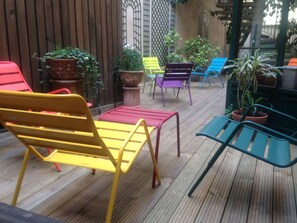 A wooden deck with colorful outdoor furniture, including a yellow bench, a red table, and a green table. - Le Relais Monceau (Paris)