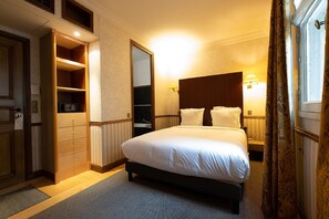 A hotel room with a large bed, a wardrobe, a mirror, and a nightstand with a lamp. - Le Relais Monceau (Paris)