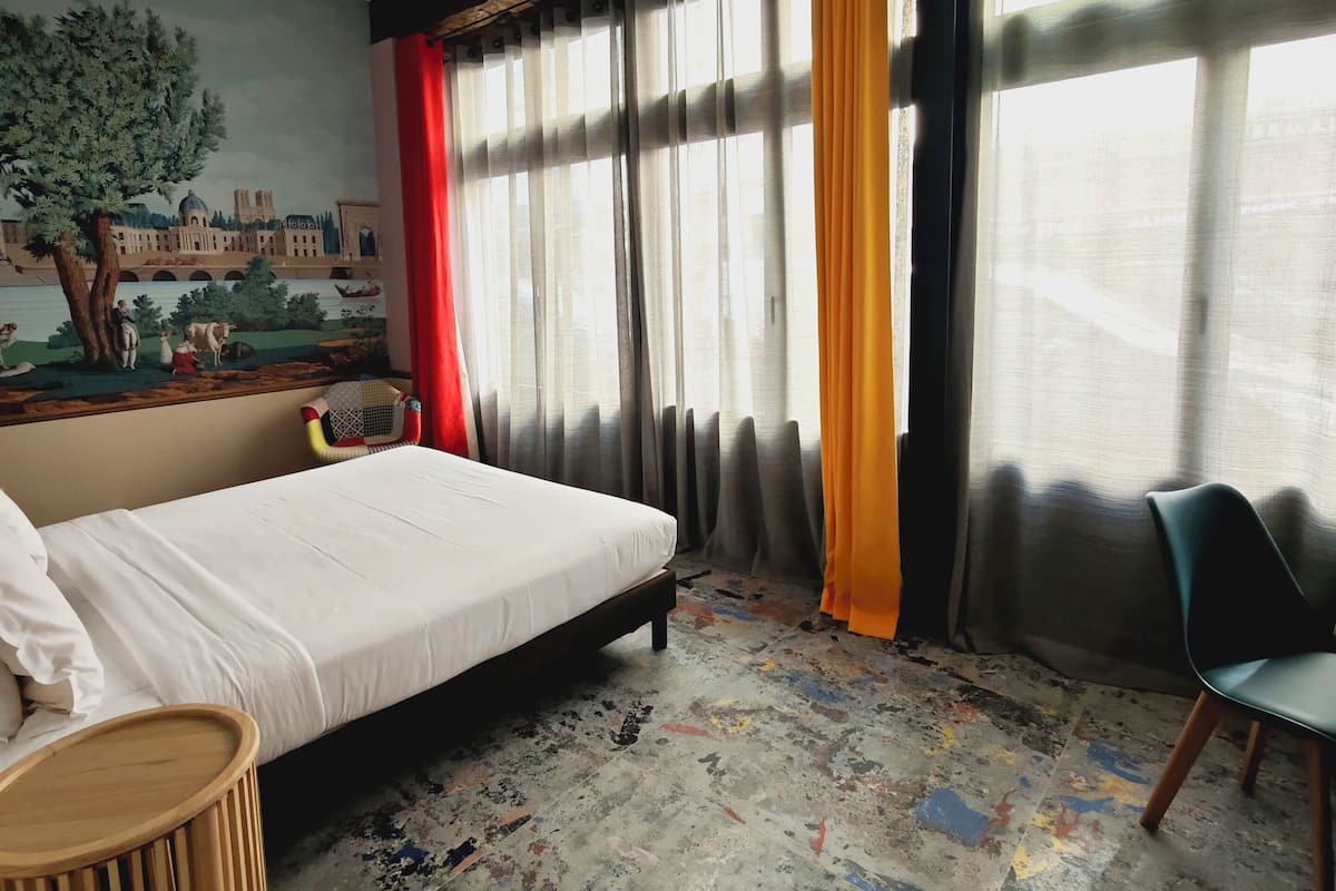Une chambre d’hôtel avec un lit, une chaise, une petite table et une fresque murale.