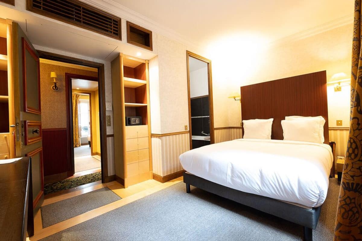 Une chambre d’hôtel comprenant un lit, une armoire, un miroir et une porte donnant sur une autre pièce.