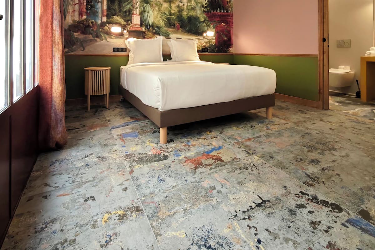 Une chambre d’hôtel avec un grand lit, une fresque murale, une petite table d’appoint et une vue sur la salle de bain.