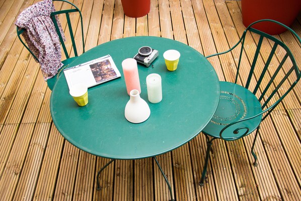 A round green table with a magazine, a camera, candles, and cups on a wooden deck. - Le Relais Monceau (Paris)