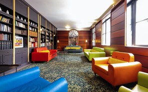 A library with bookshelves, a red sofa, a green sofa, a blue sofa, and a patterned carpet. - Le Relais Monceau (Paris)
