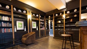 A library with bookshelves, a reading chair, and bar stools. - Le Relais Monceau (Paris)