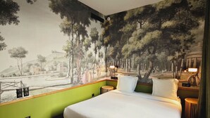 A hotel room with a large bed, a mural of a forest scene, a view of a body of water, and a small round table with a lamp. - Le Relais Monceau (Paris)