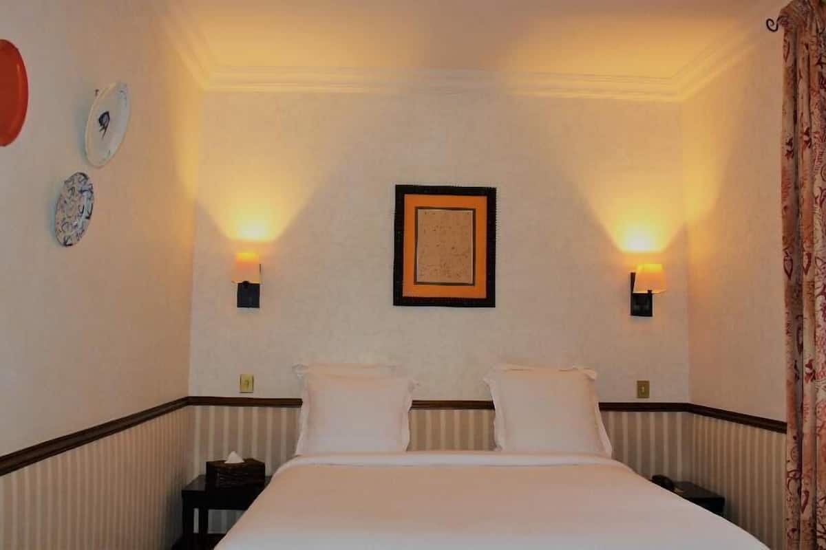 Une chambre d’hôtel avec un lit, deux tables de chevet, un tableau encadré au mur et deux lampes fixées au mur.
