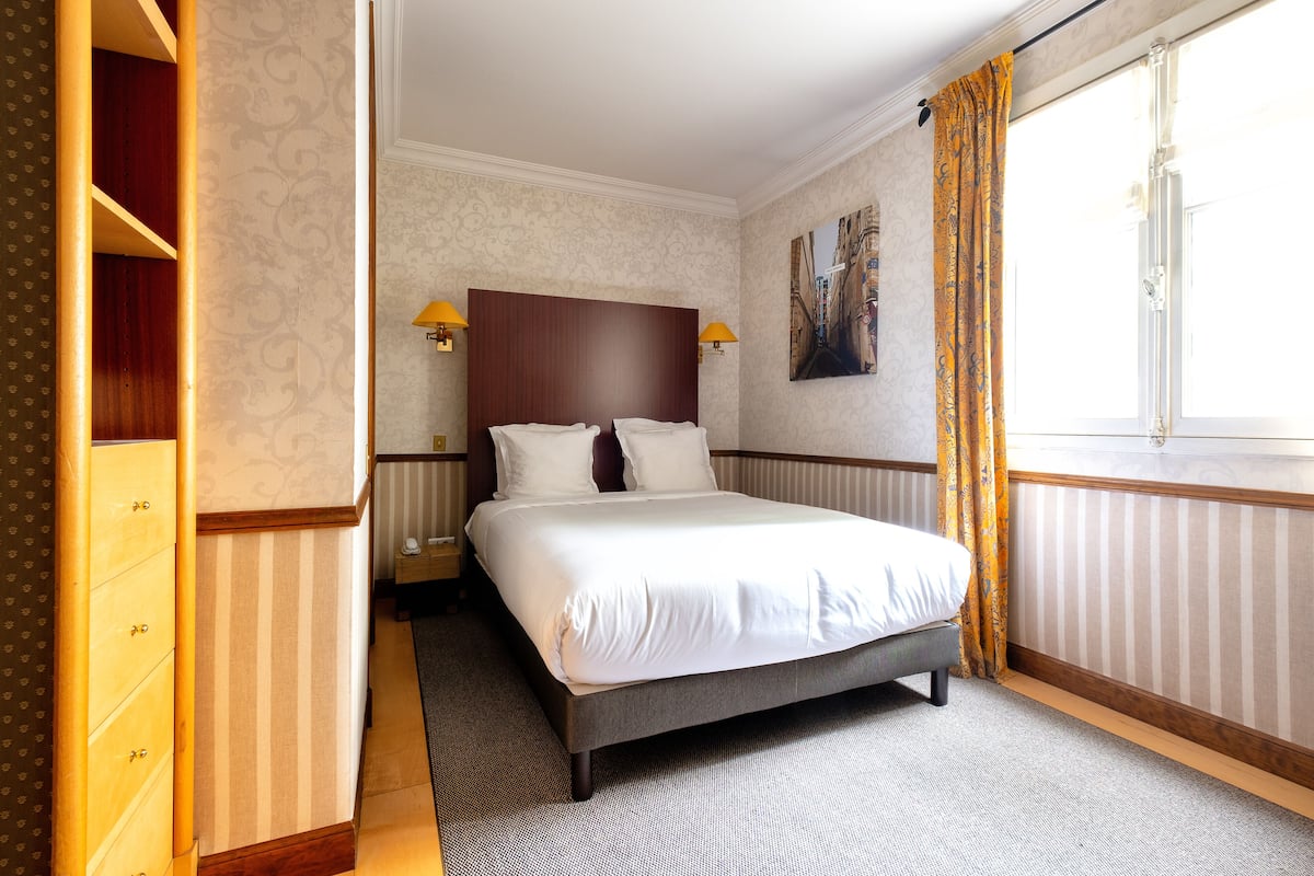 Une chambre d’hôtel avec un grand lit, deux tables de chevet avec des lampes, une armoire et une fenêtre avec des rideaux.