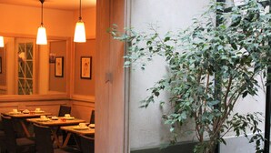 A dining area with tables set for service, a large potted plant, and hanging pendant lights. - Le Relais Monceau (Paris)