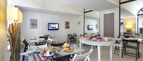 A dining area with multiple tables and chairs, equipped with breakfast items and a television.