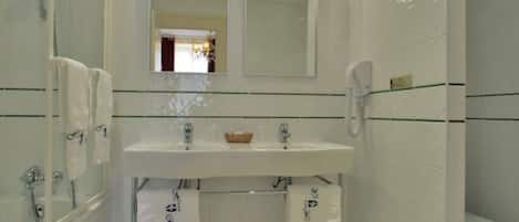 Un baño moderno con lavamanos, espejo y inodoro blancos. Cuenta con dos toalleros y una mampara de vidrio para la ducha.
