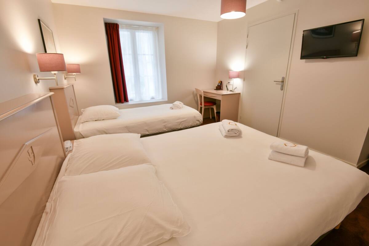 A hotel room with two beds, a desk, a chair, a TV, and a window with curtains.