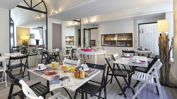 A hotel dining area with multiple tables and chairs, breakfast items, and a kitchen in the background.