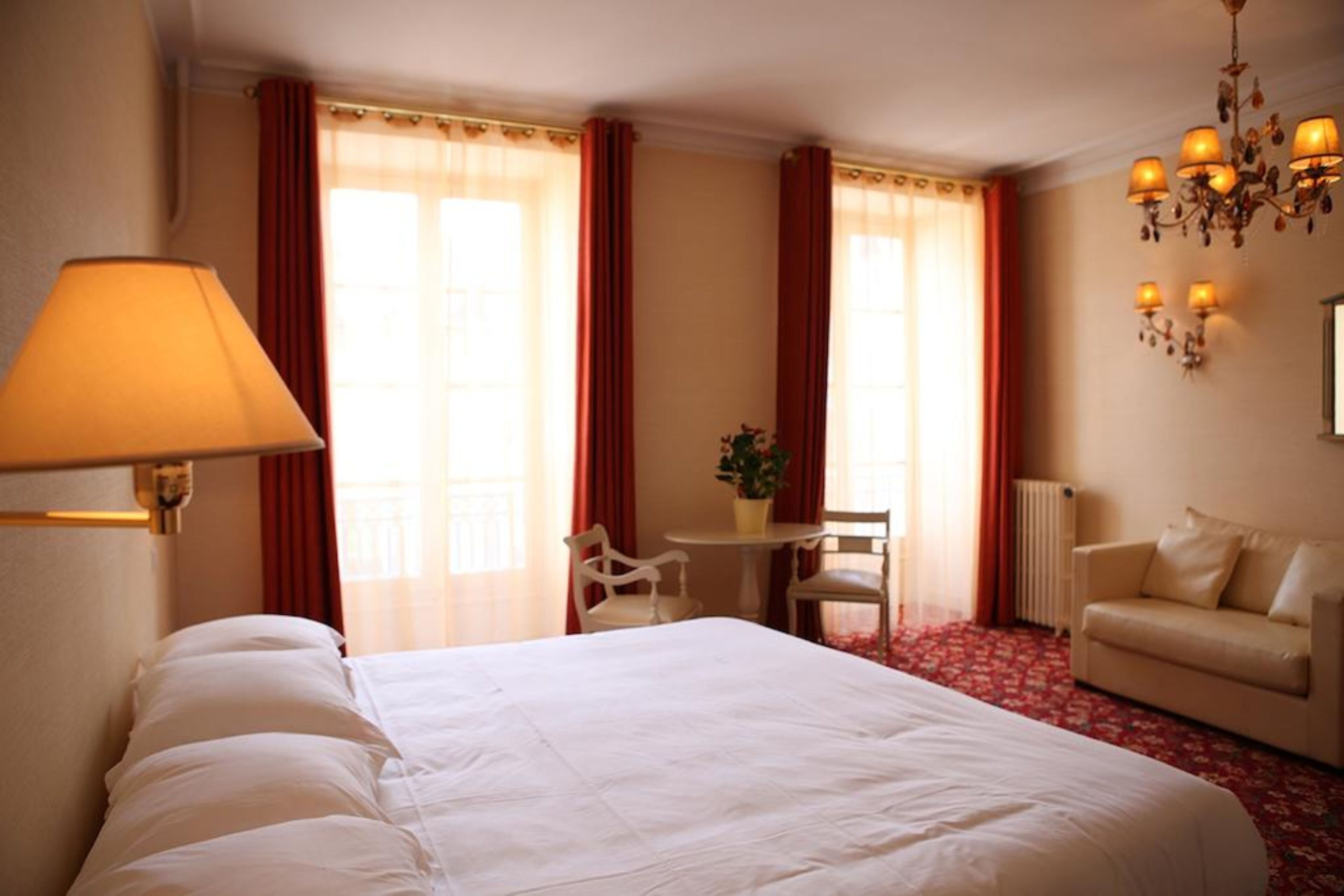 A hotel room with a large bed, a desk with a chair, a sofa, and a chandelier.