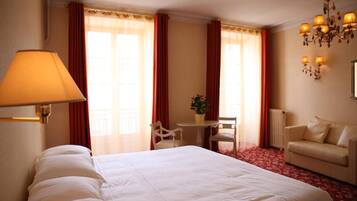 A hotel room with a large bed, a desk with a chair, a sofa, and a chandelier.
