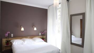Habitación de hotel con una cama grande, dos lámparas de noche, un espejo y una ventana con cortinas.