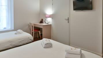 Quarto de hotel com duas camas, uma escrivaninha com cadeira, televisão na parede e uma luminária.