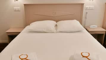 Habitación de hotel con una cama individual, dos almohadas blancas, dos mesitas de noche con lámparas, un cuadro en la pared y dos toallas con un logo.