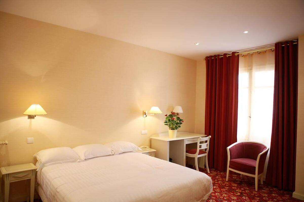 A hotel room with a bed, a desk, a chair, and a window with curtains.
