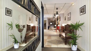 A hotel lobby with a central seating area, a staircase, and a mirrored wall with framed pictures.